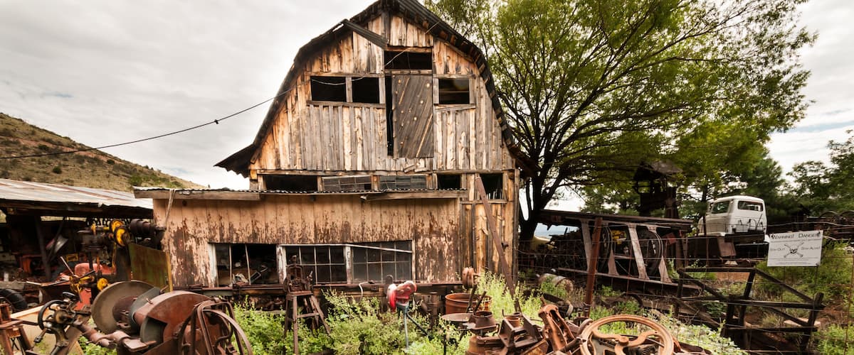 An abandoned barn surrounded by overgrown vegetation and rusted machinery.