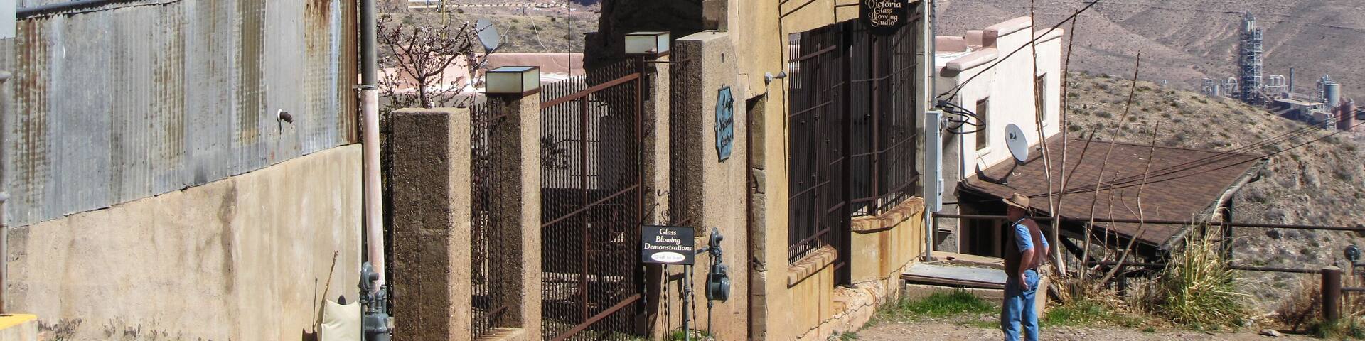 A dilapidated building with a metal gate, a person standing nearby, and a mountainous landscape in the background.