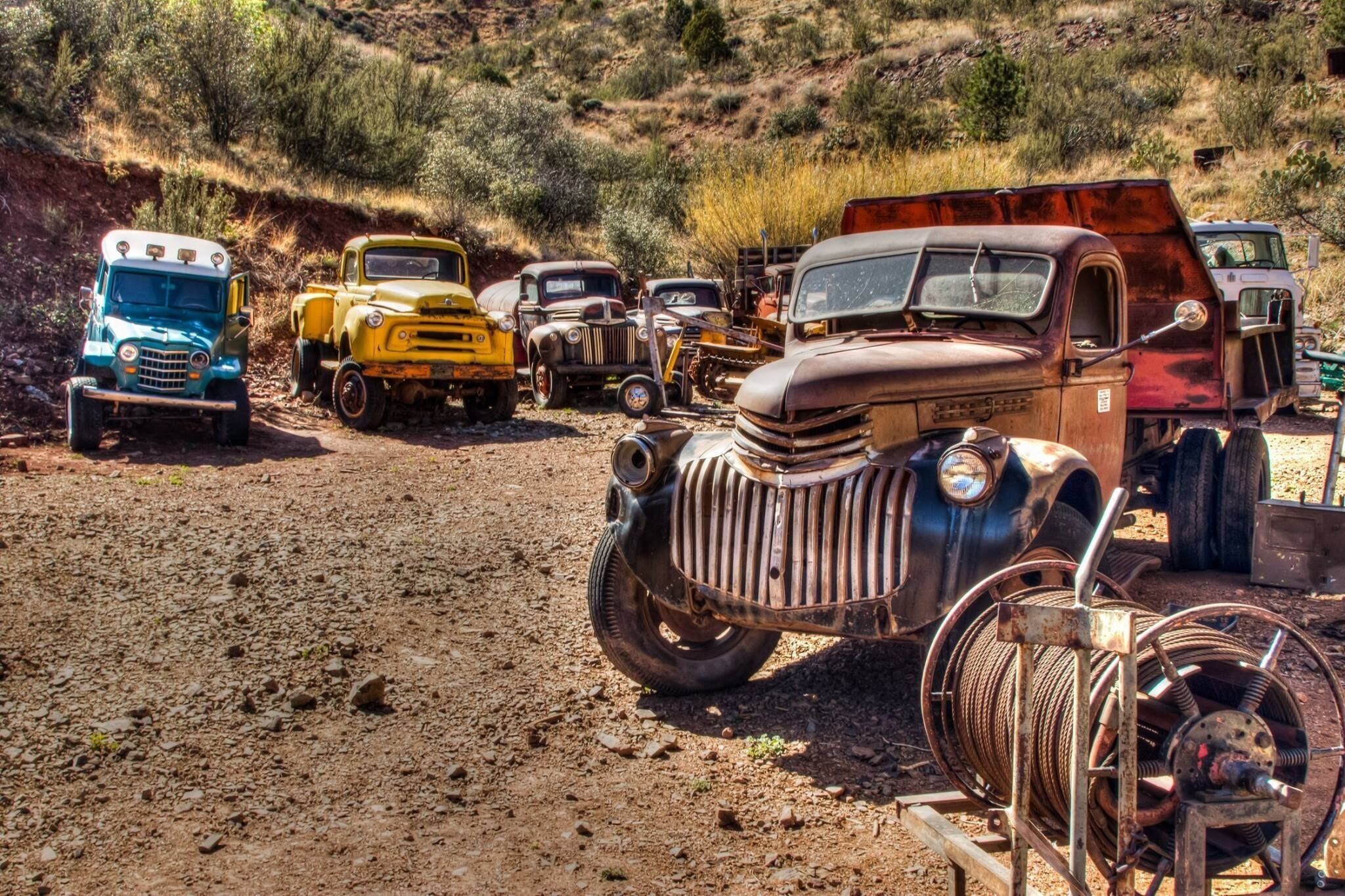 A collection of vintage trucks parked on a dirt road in a hilly, arid landscape.