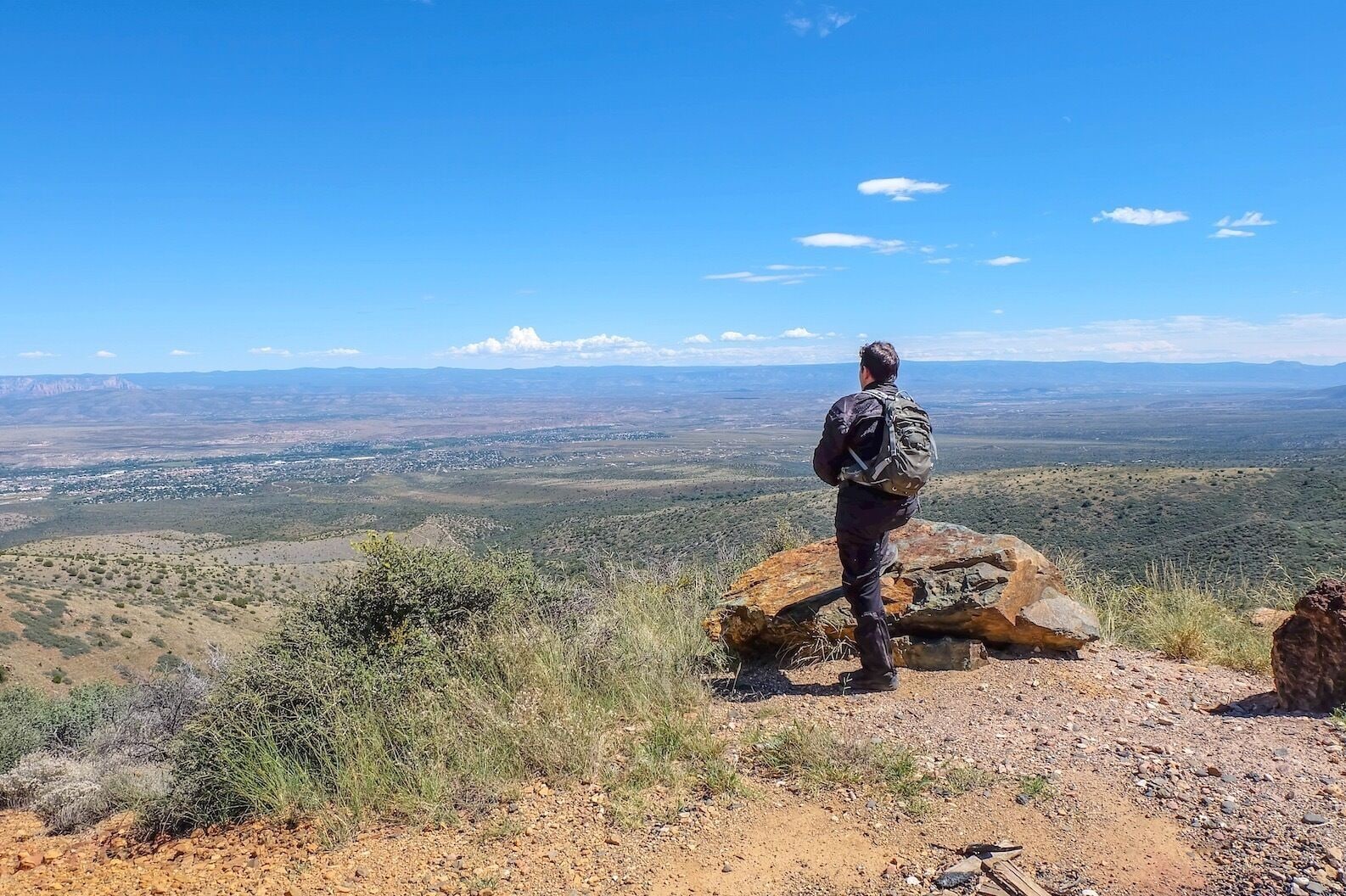 A person standing on a rocky outcrop overlooking a vast landscape with sparse vegetation and distant hills.