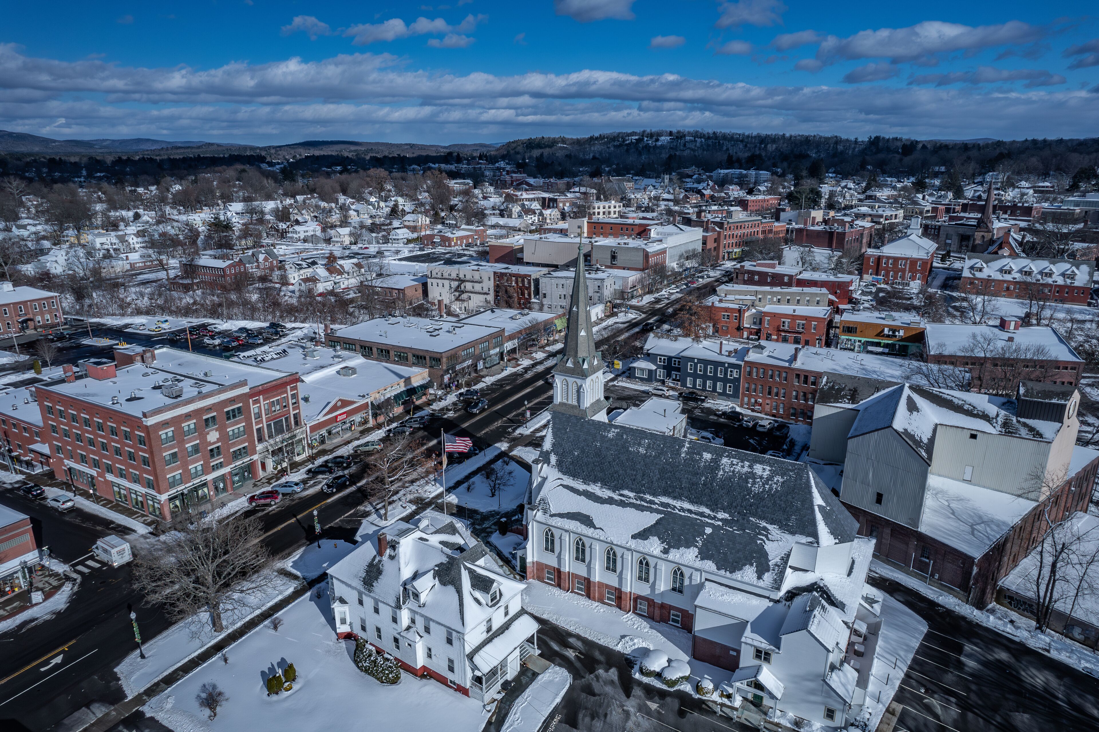 A snow-covered town with a prominent church steeple, red brick buildings, and a clear blue sky.