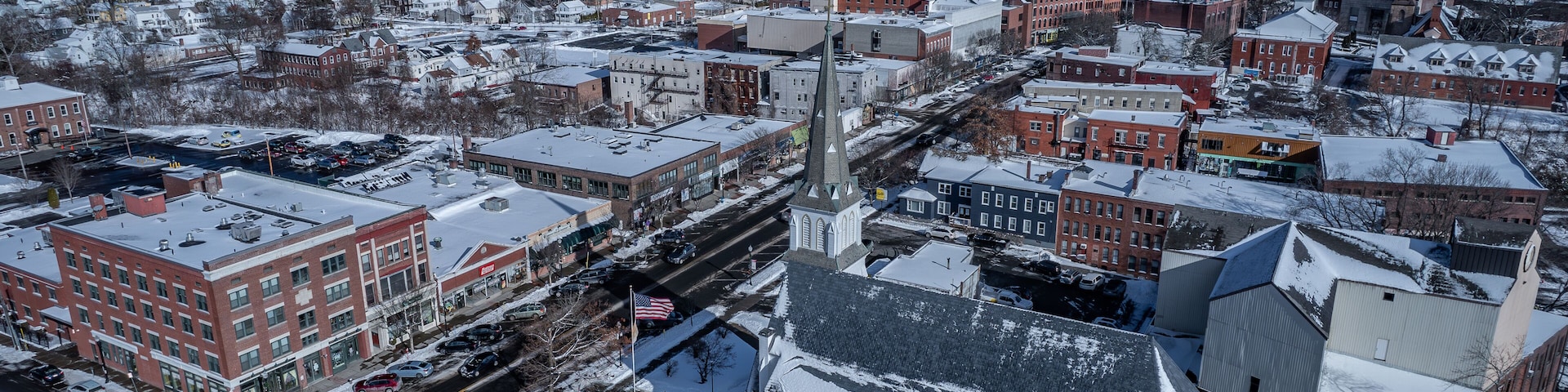 A snow-covered town with a prominent church steeple, red brick buildings, and a clear blue sky.