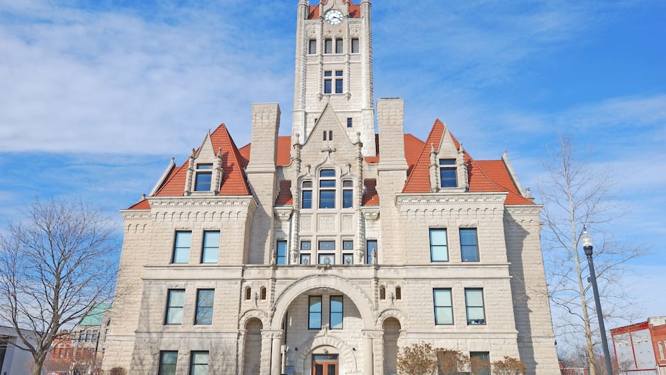 A large, historic building with a clock tower, arched windows, and a red-tiled roof.