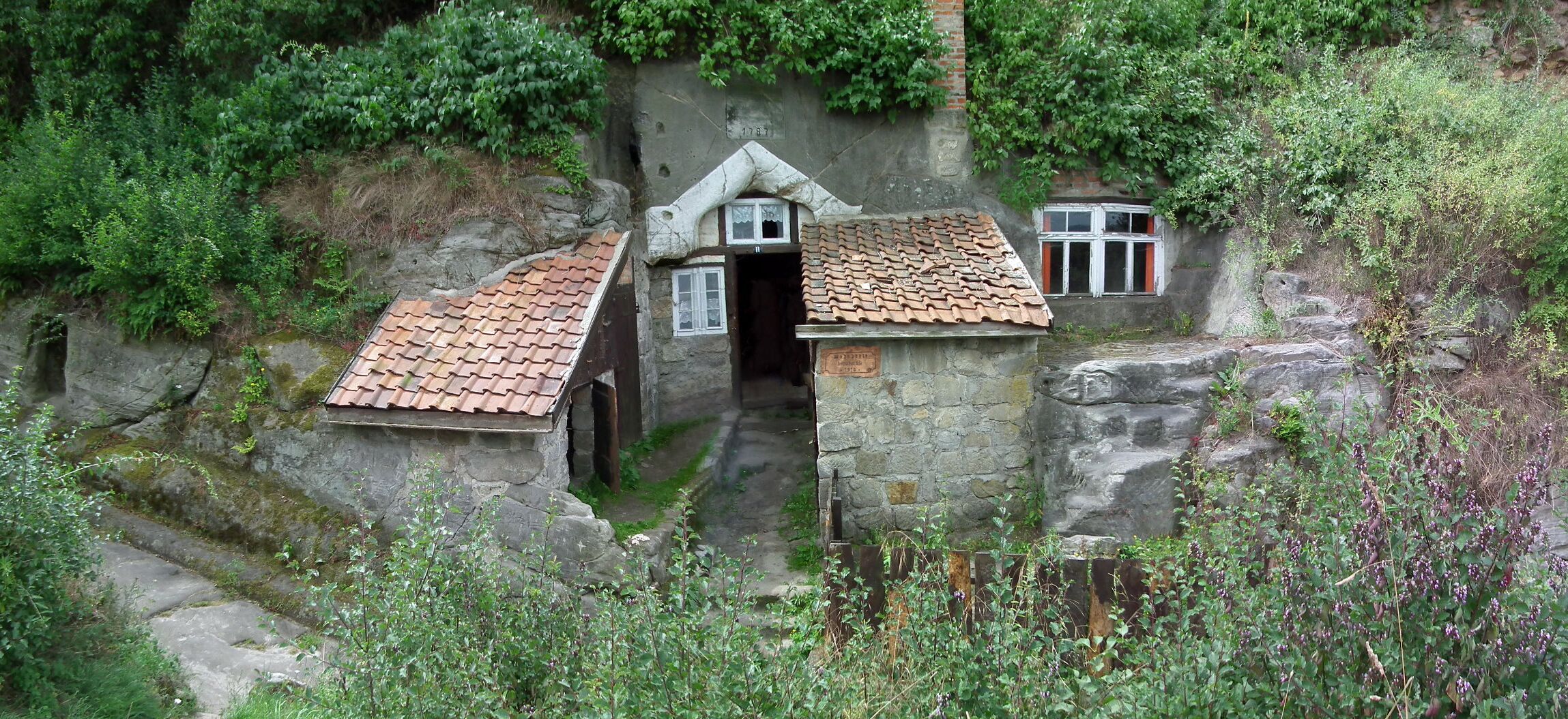 A stone house with a tiled roof nestled in a rocky hillside.