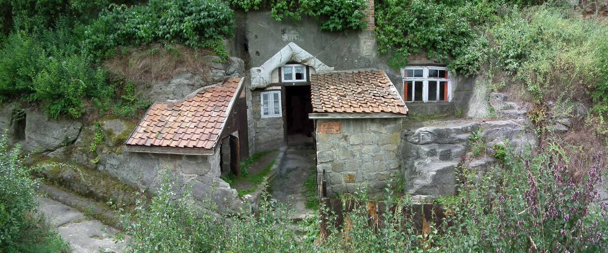 A stone house with a tiled roof nestled in a rocky hillside.
