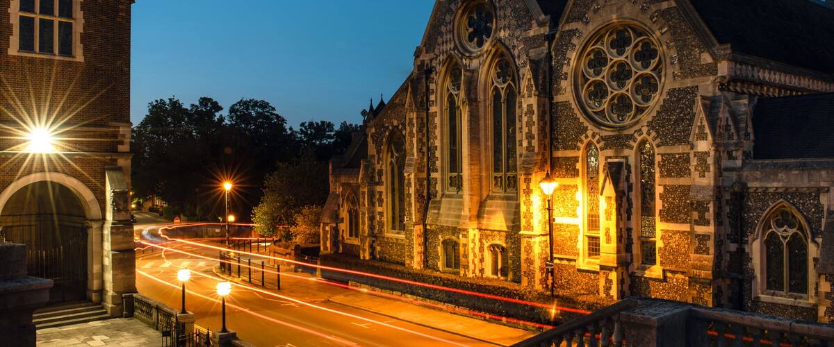A historic church with a tall spire and large stained glass windows, illuminated by street lamps.