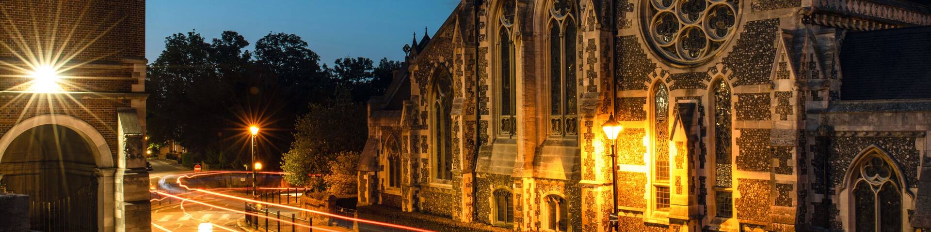 A historic church with a tall spire and large stained glass windows, illuminated by street lamps.