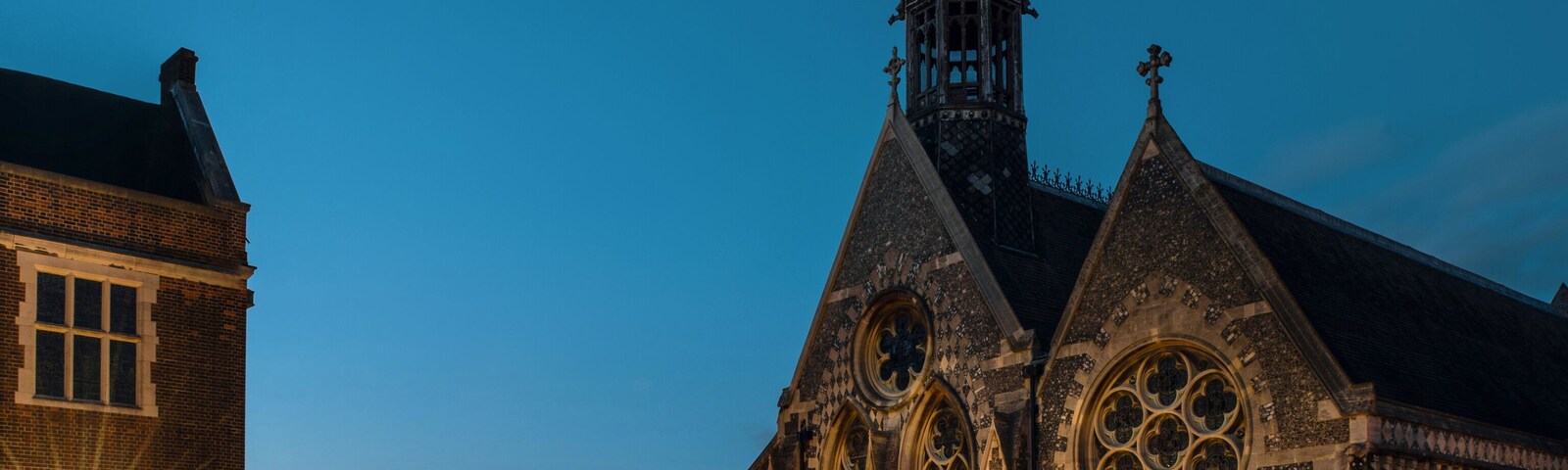 Uma igreja histórica com uma torre alta e grandes vitrais, iluminada por postes de luz.