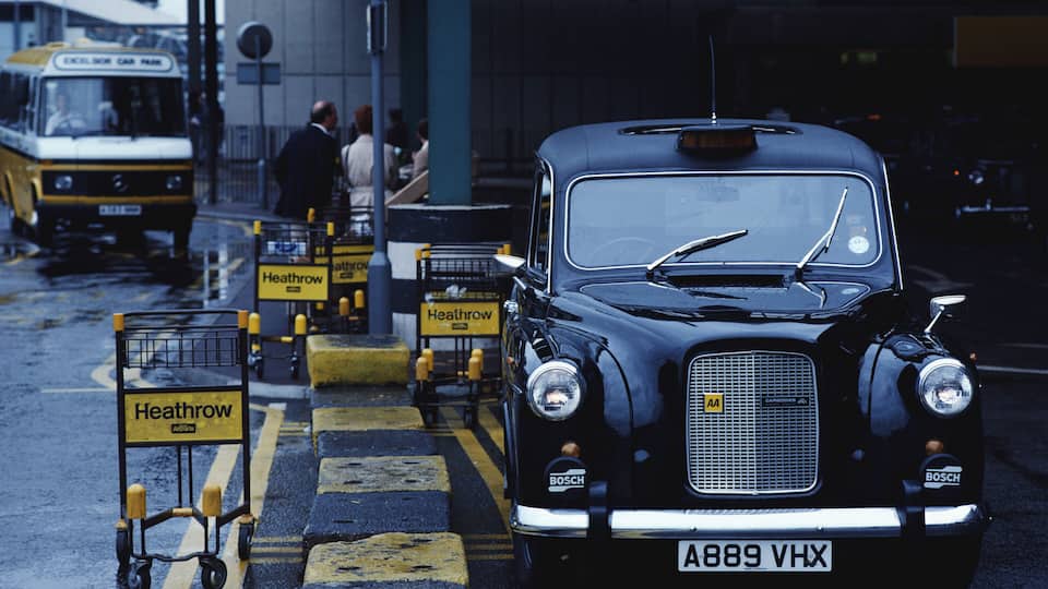 A vintage black car with a license plate A889 VHX parked at a bus station.