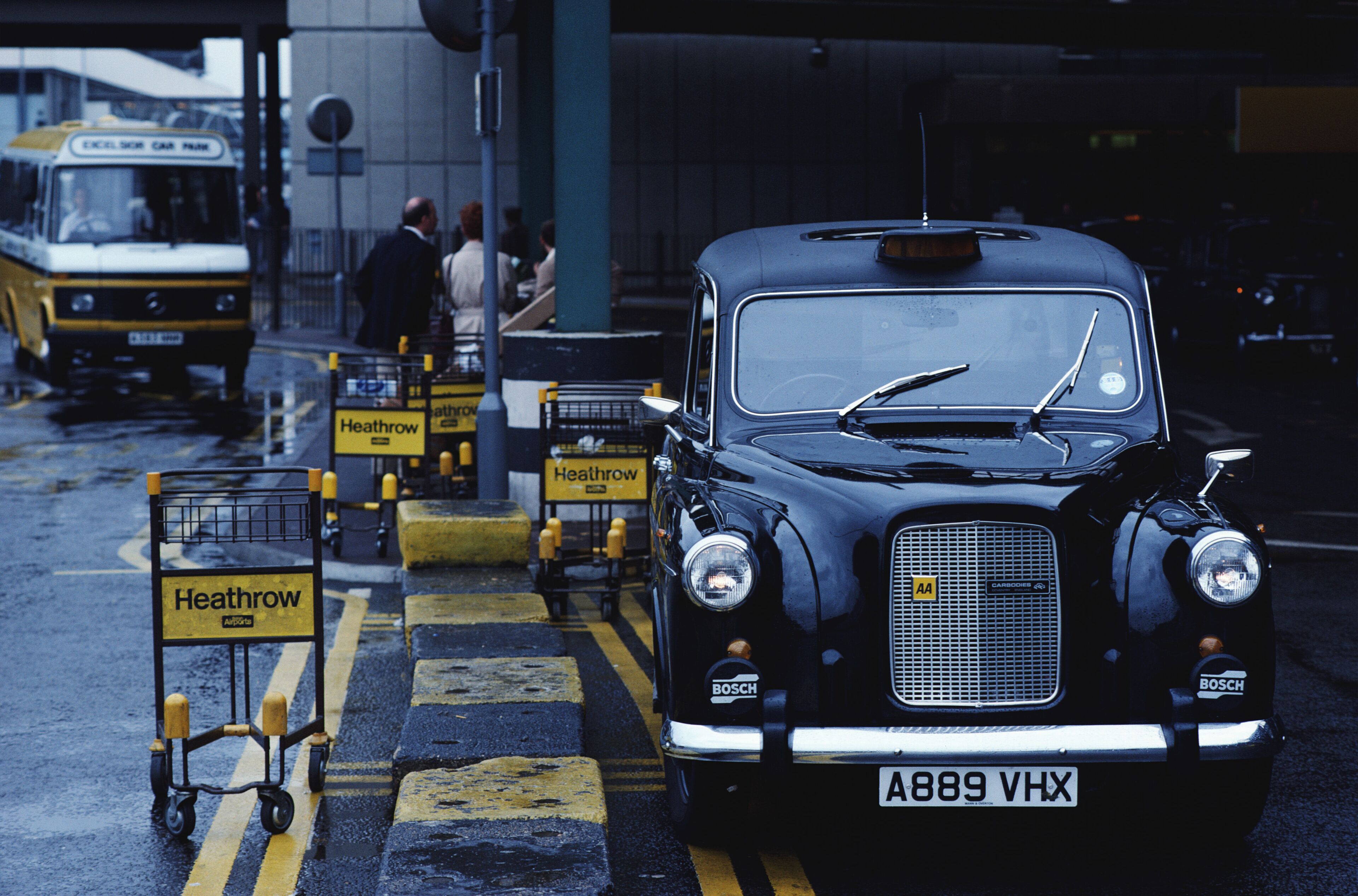 A vintage black car with a license plate A889 VHX parked at a bus station.