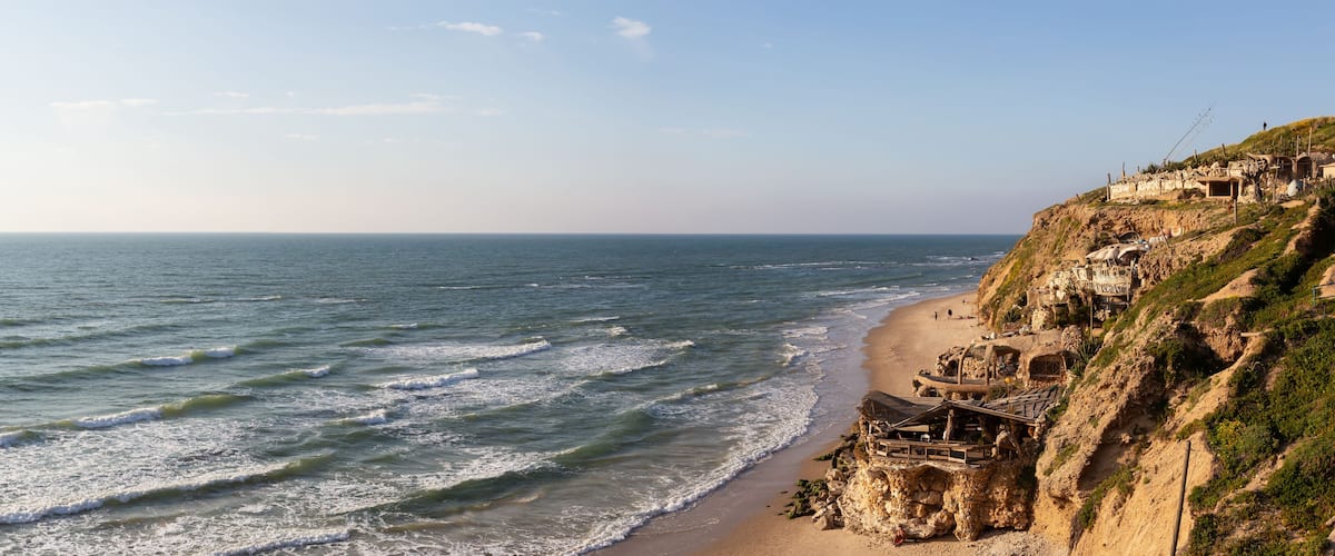 A coastal cliff with ancient ruins and a beach.