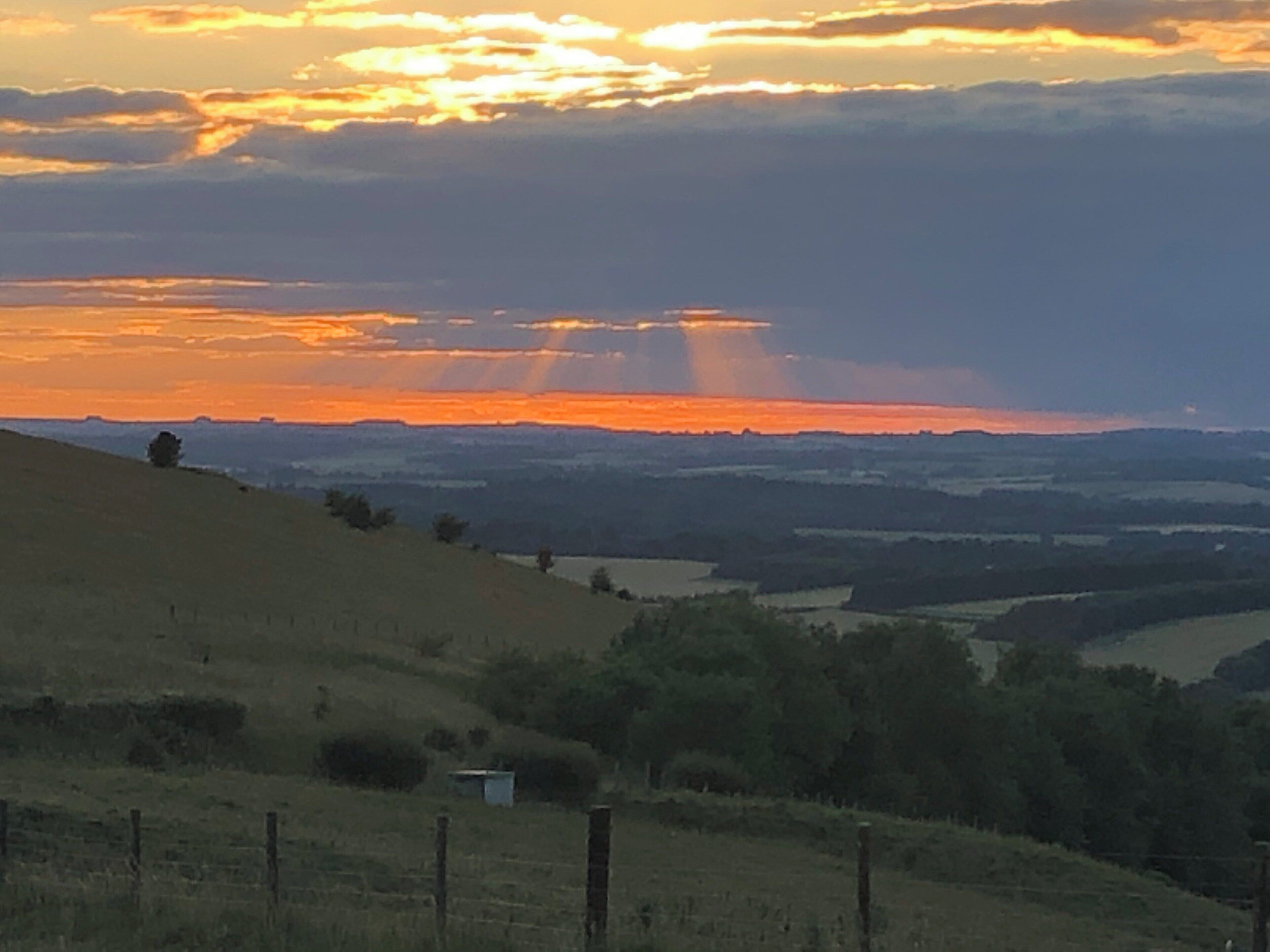 A sunset over rolling hills with a small building in the foreground.