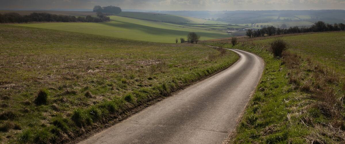 A winding country road through rolling green fields under a cloudy sky.