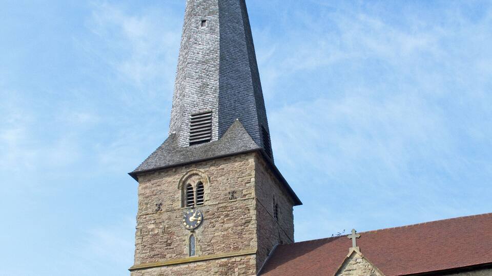 A church with a tall, pointed steeple and a stone clock tower.