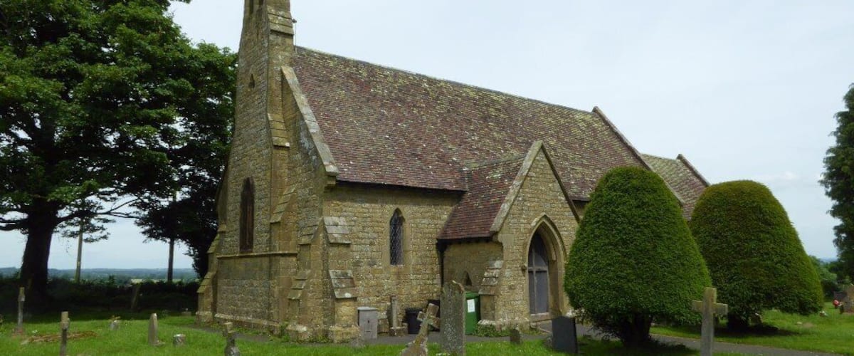 A stone church with a tall steeple, surrounded by a cemetery with headstones.