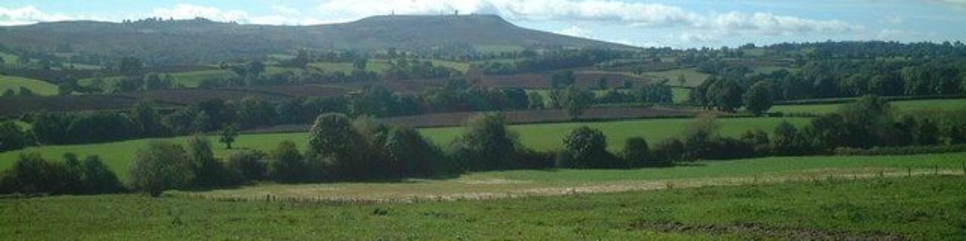Paisaje rural con colinas onduladas, campos y una cadena montañosa distante bajo un cielo despejado.