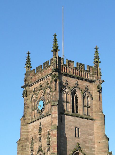 A tall, historic tower with a clock, intricate stone carvings, and a flagpole.