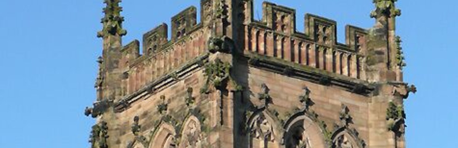A tall, historic tower with a clock, intricate stone carvings, and a flagpole.