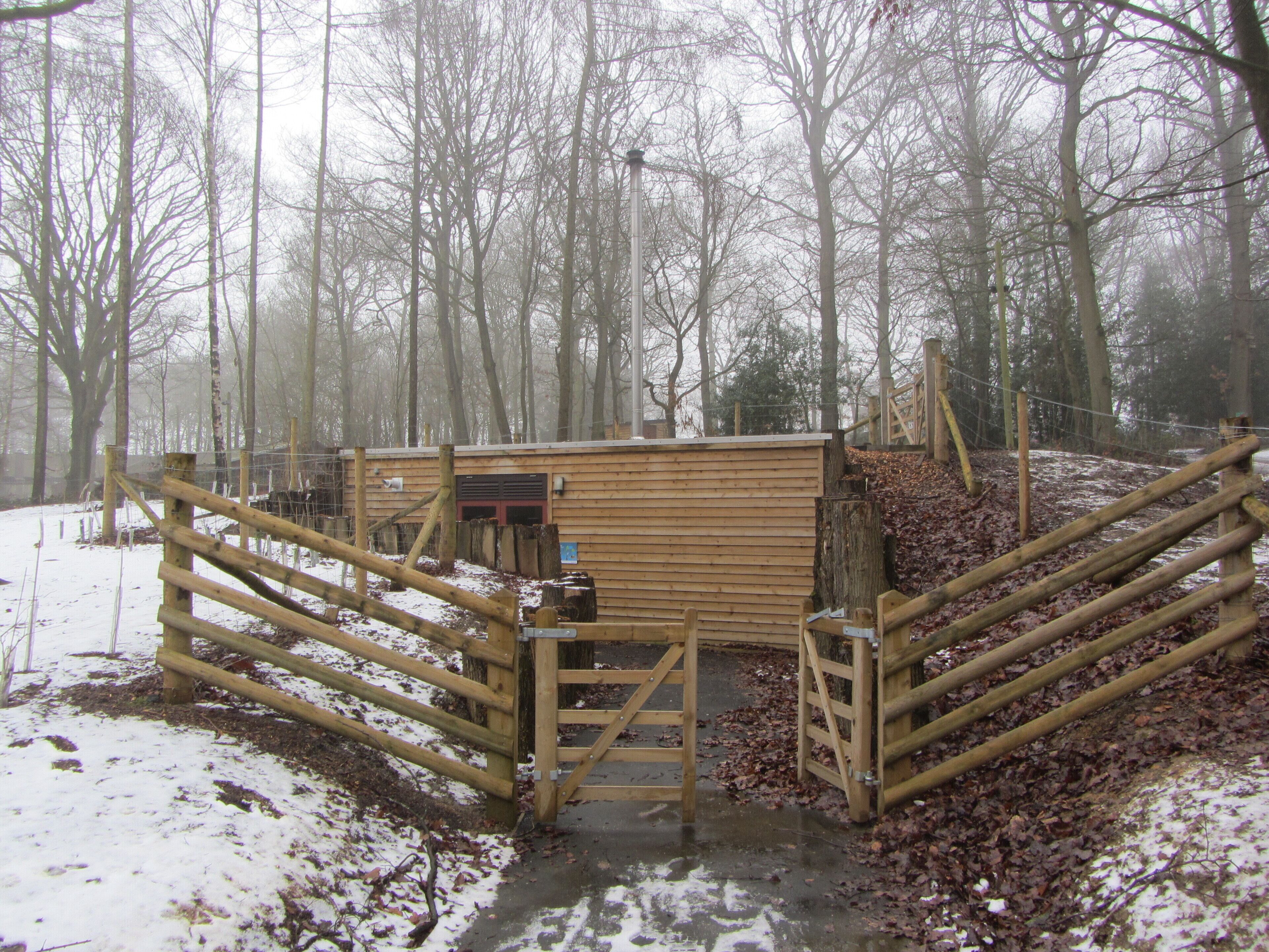 A wooden structure with a gate, surrounded by trees and covered in snow.
