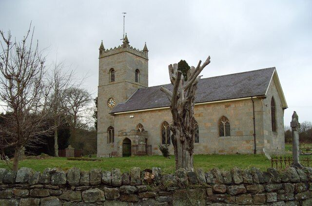 A stone church with a bell tower and a large tree in front.
