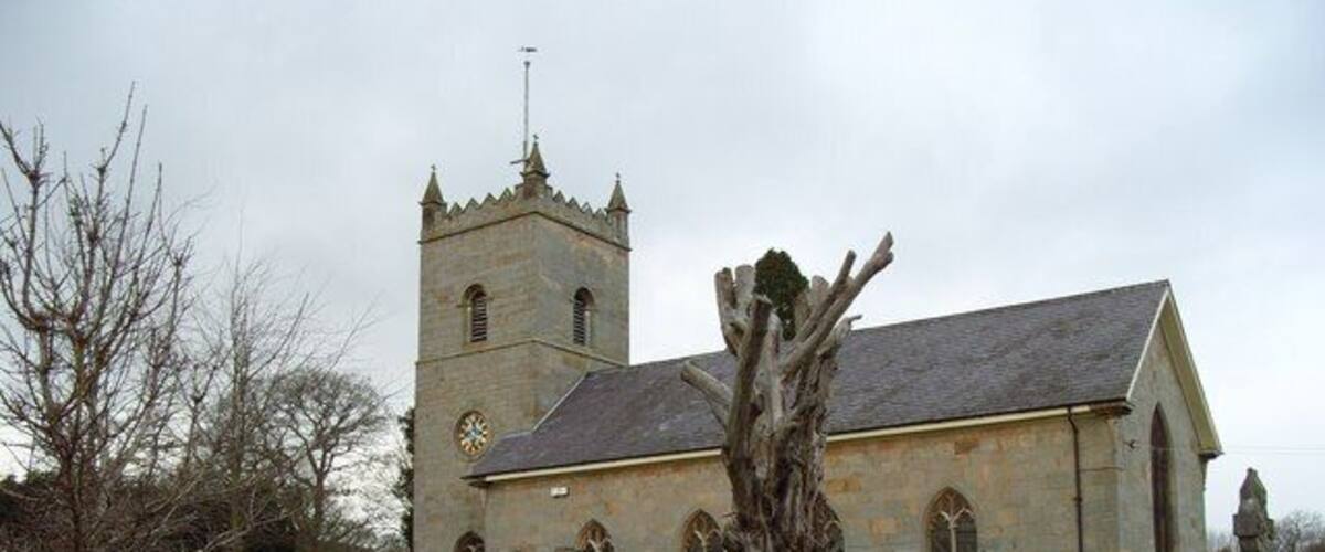 A stone church with a bell tower and a large tree in front.