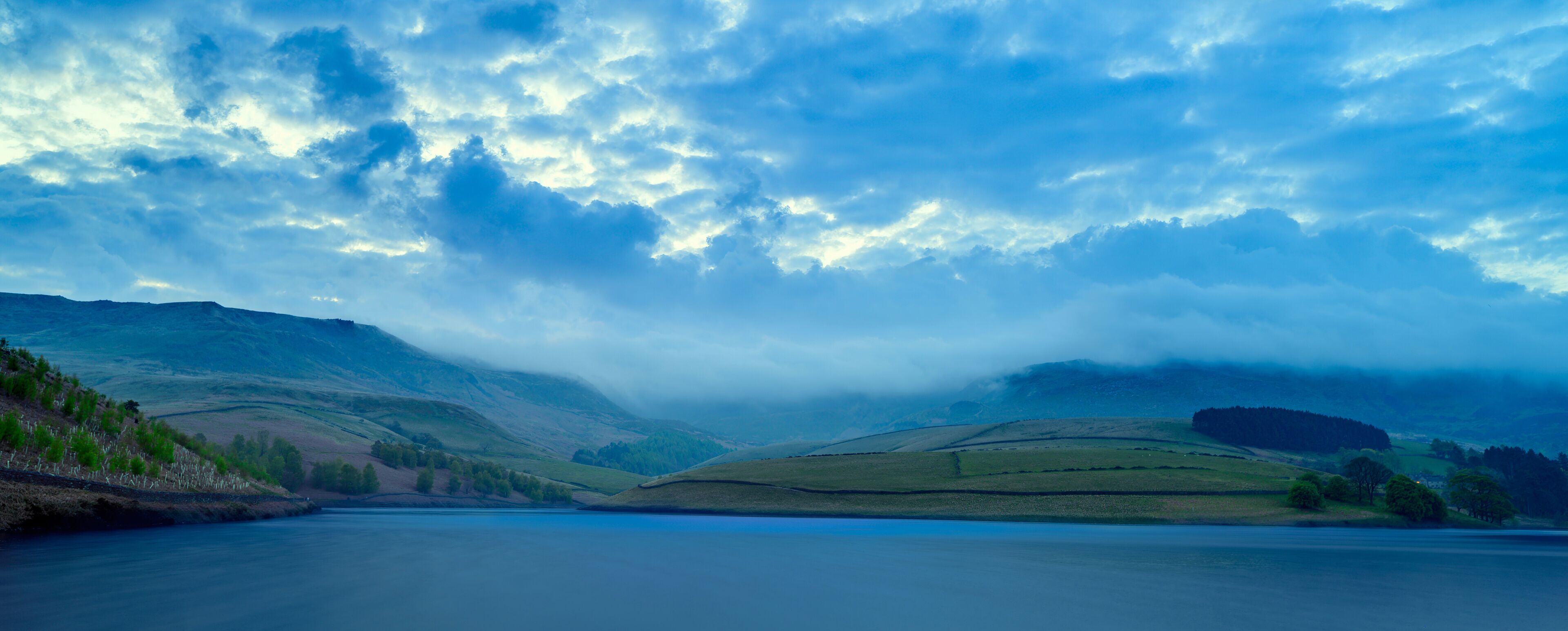 A lake surrounded by rolling hills and a cloudy sky.