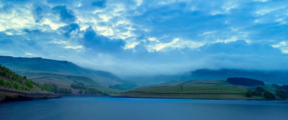 A lake surrounded by rolling hills and a cloudy sky.