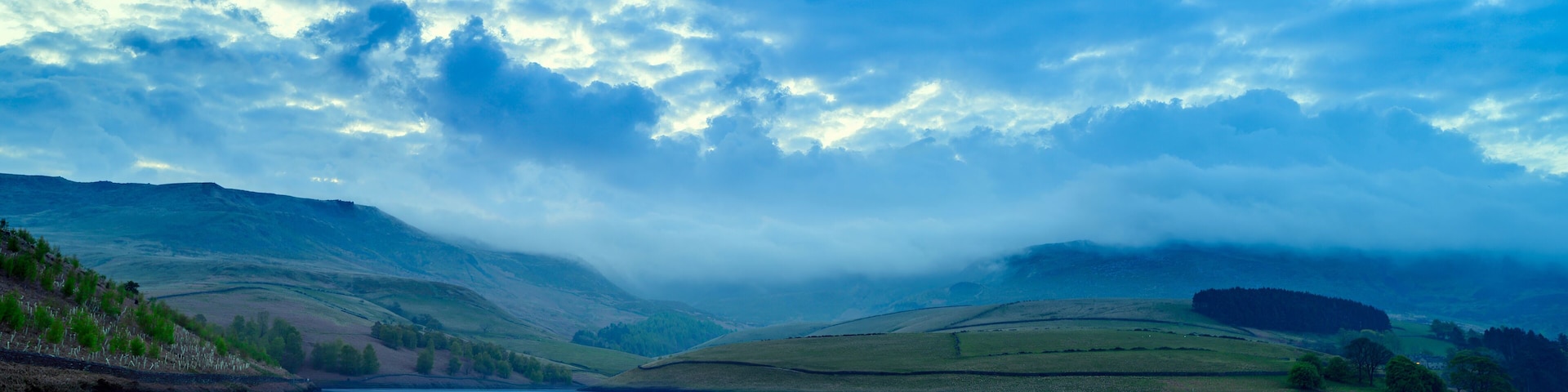 A lake surrounded by rolling hills and a cloudy sky.