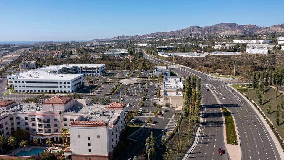 A cityscape with modern buildings, a wide road, and mountains in the background.