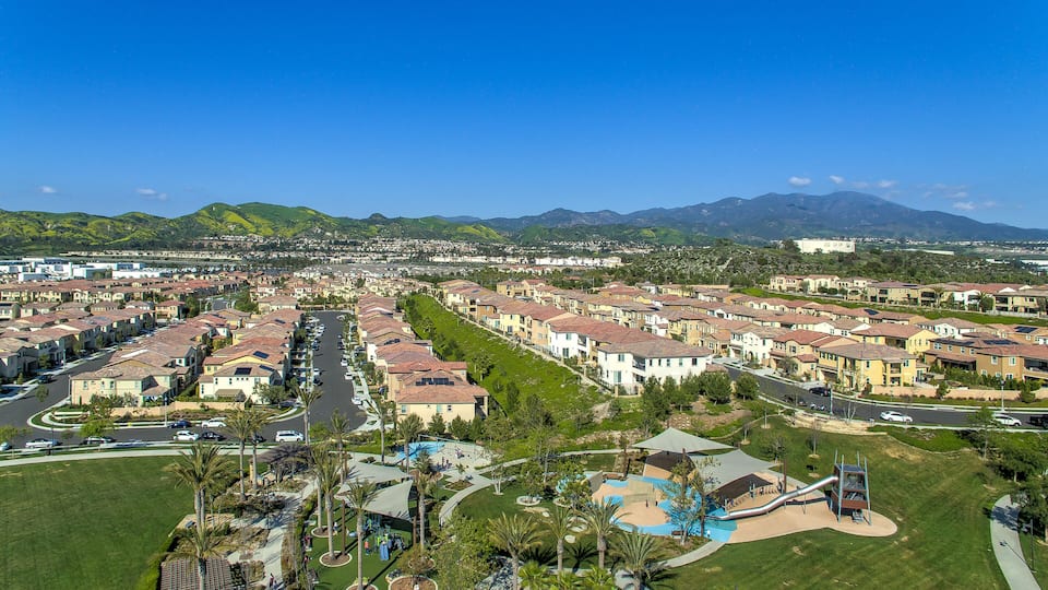 A residential area with a central park, playground, and a mountain range in the background.