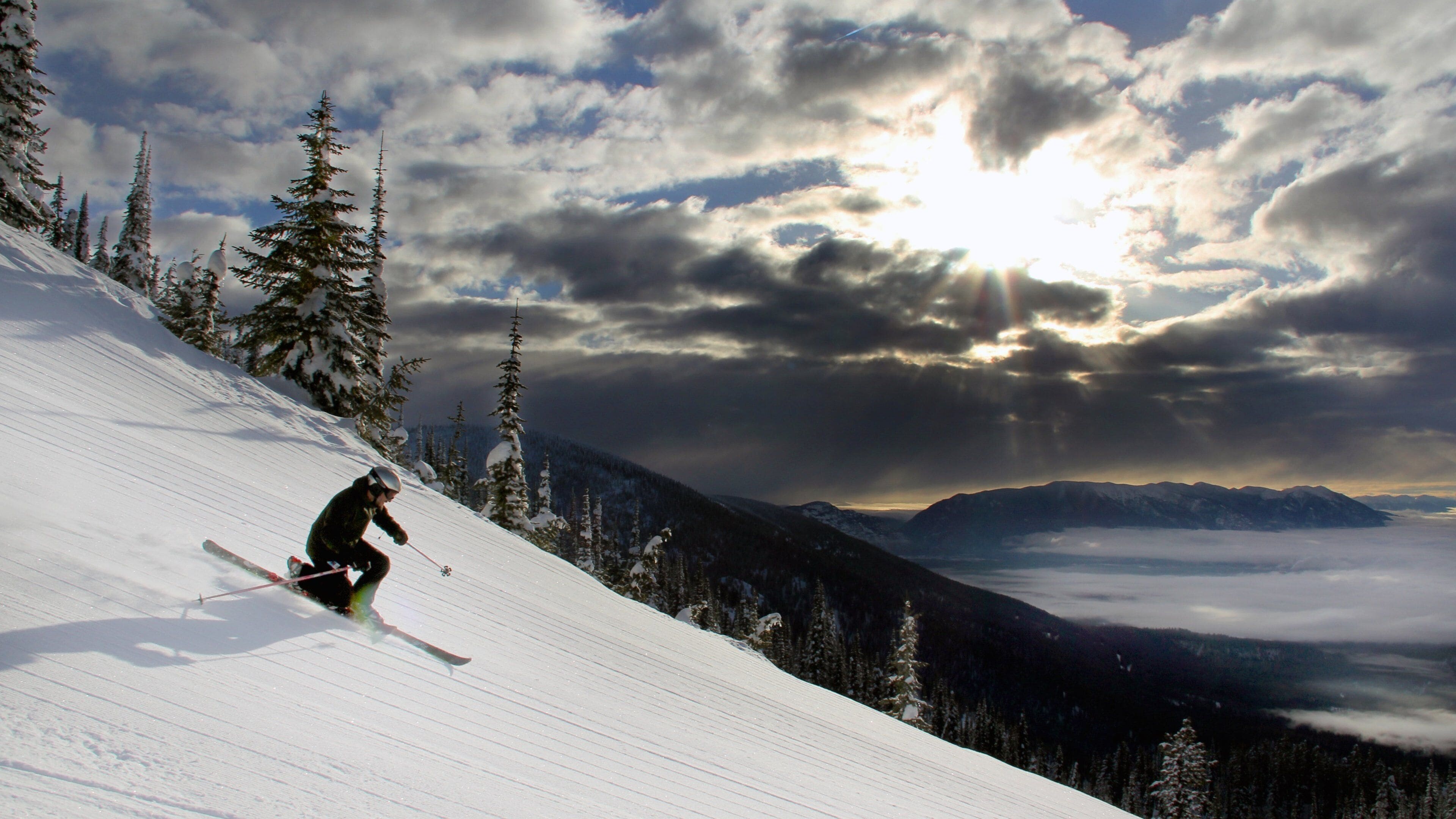 A skier on a snowy slope with a mountain range and clouds in the background.