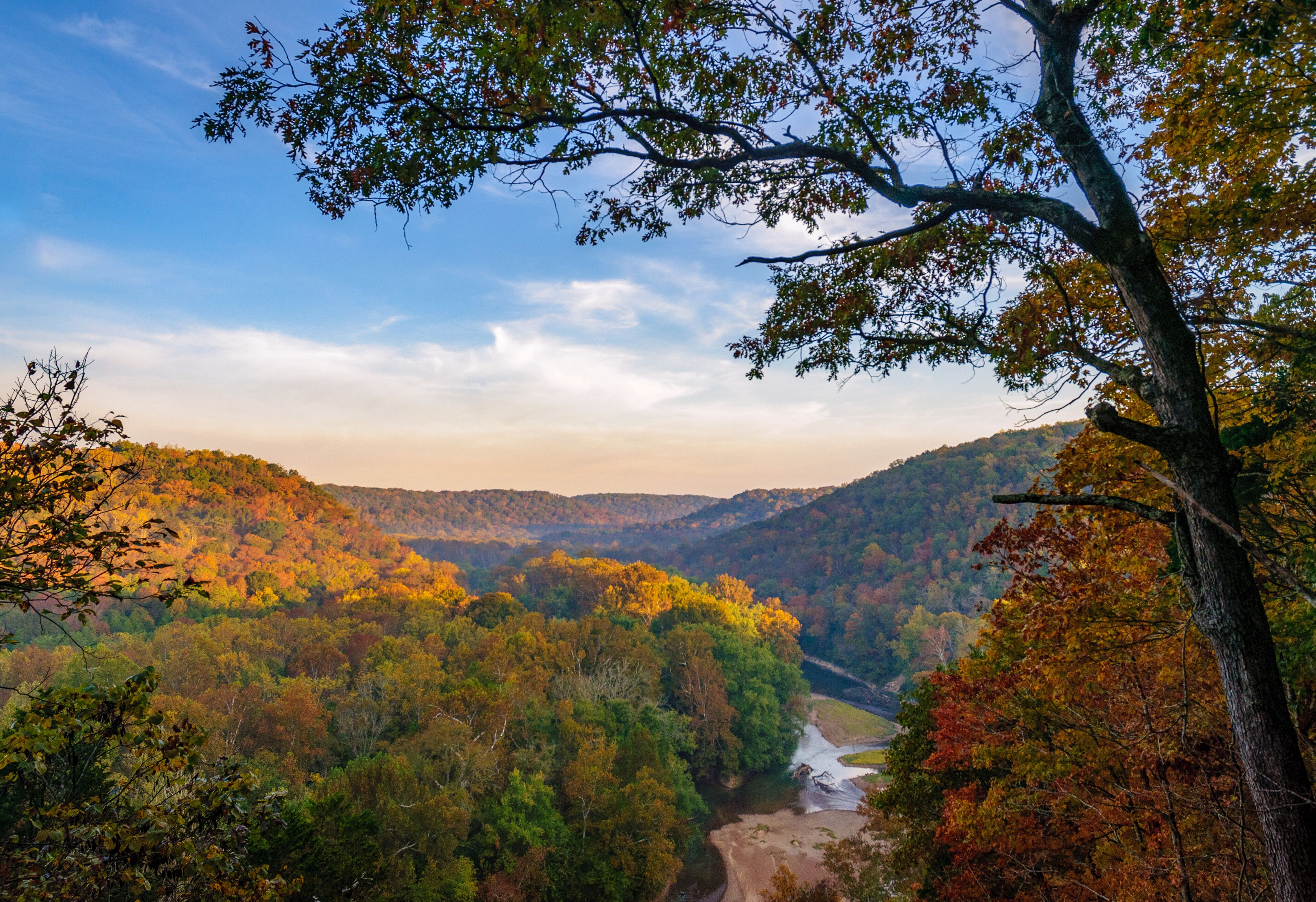 A valley with a river, surrounded by autumn-colored trees and hills.