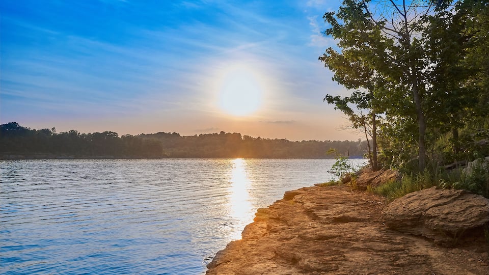 A sunset over a calm lake with rocky shores and trees.