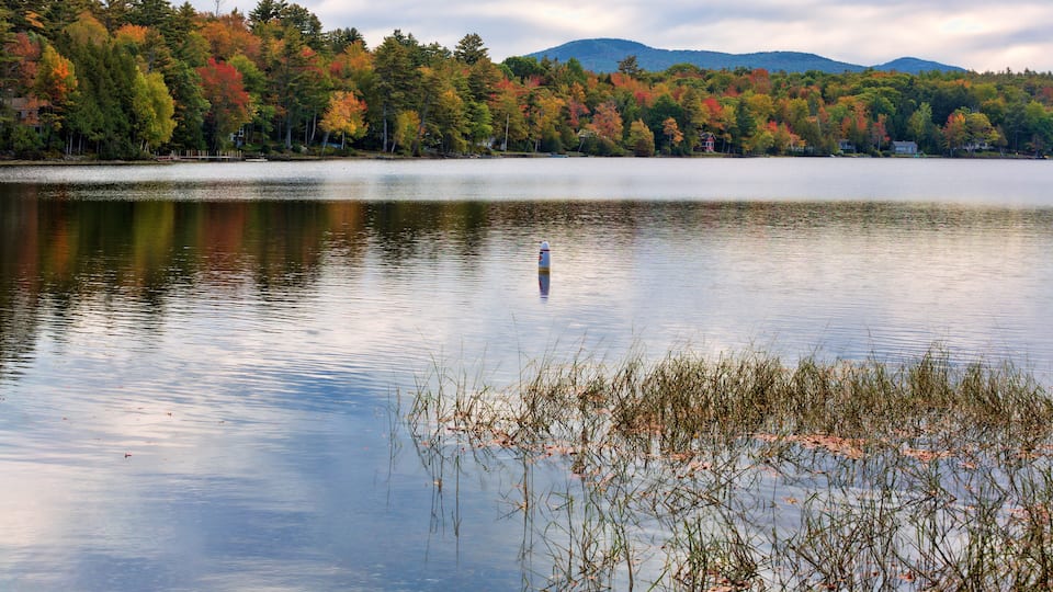A calm lake with autumn foliage and a distant mountain range.