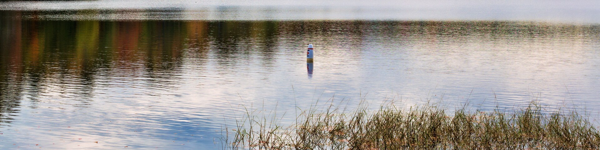 Un lago tranquilo con follaje otoñal y una cadena montañosa distante.