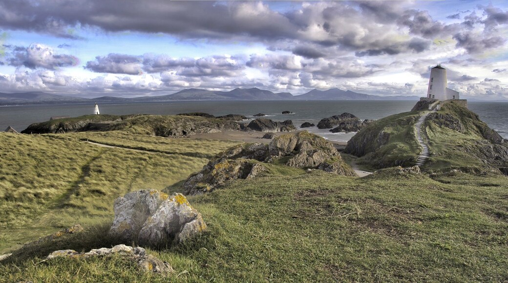 A coastal landscape with a lighthouse, rocky terrain, grassy hills, and a distant mountain range.