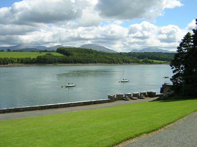 A calm lake with boats, grassy banks, and mountains in the background.