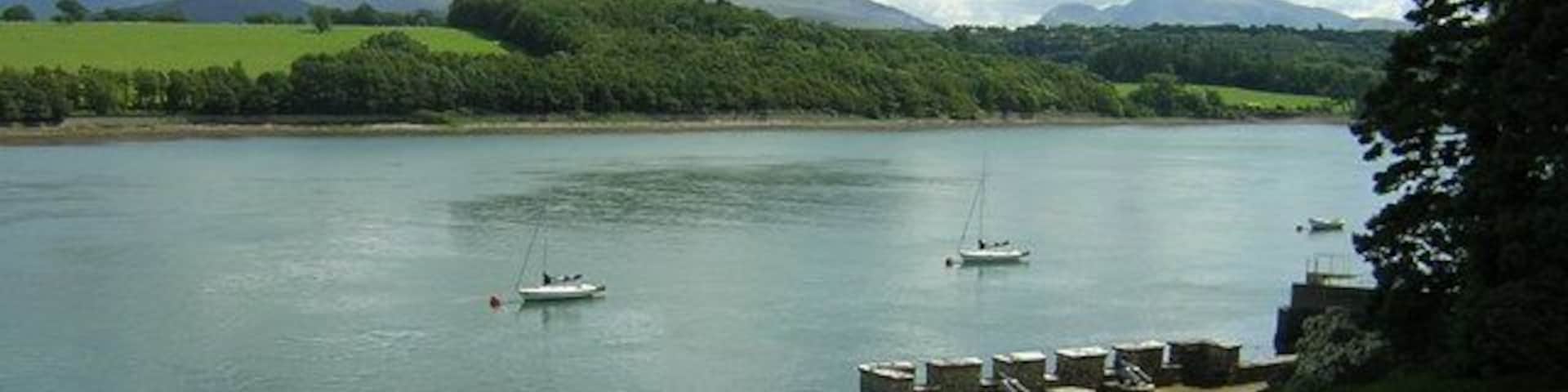 A calm lake with boats, grassy banks, and mountains in the background.
