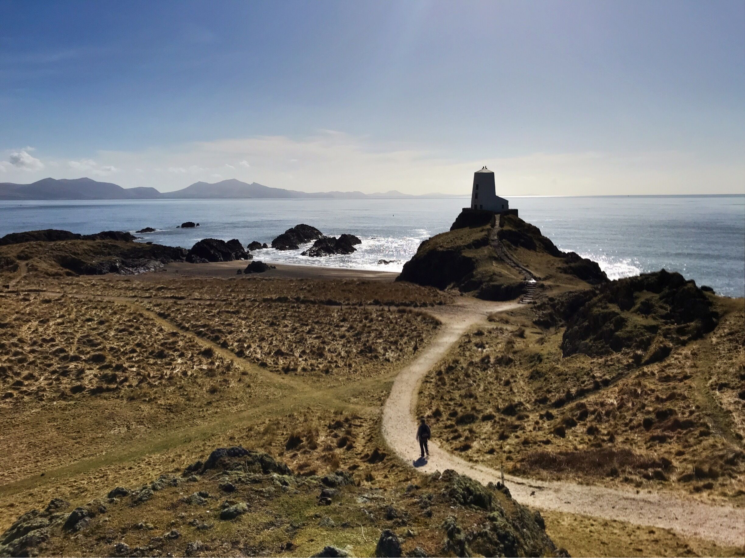 A coastal landscape with a lighthouse on a rocky outcrop, a dirt path leading to it, and the ocean in the background.