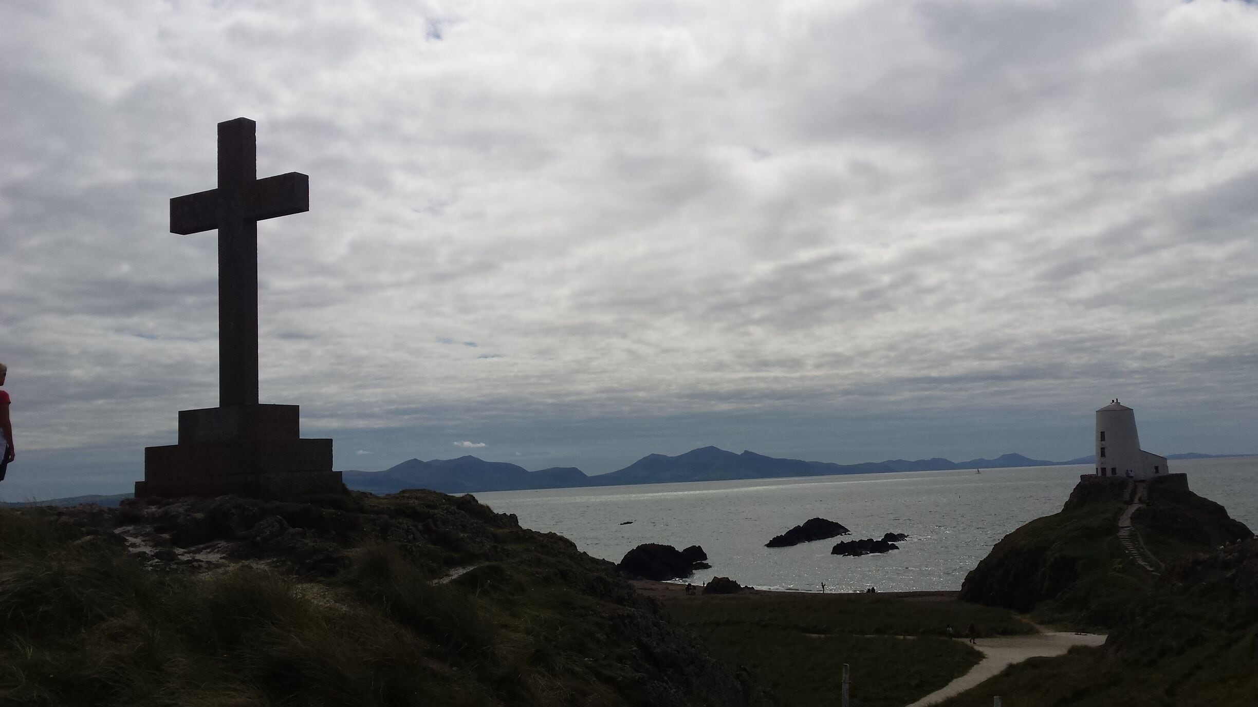A cross monument, a lighthouse, and a coastal landscape with mountains in the background.