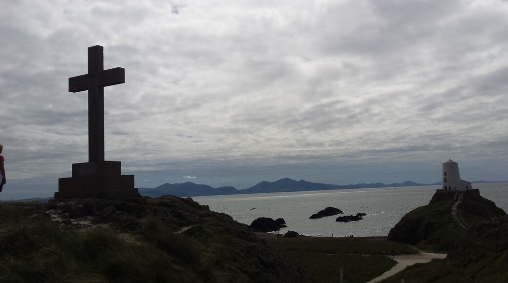 A cross monument, a lighthouse, and a coastal landscape with mountains in the background.