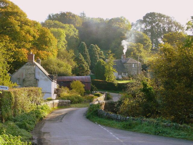 A narrow rural road flanked by lush greenery and traditional stone houses.