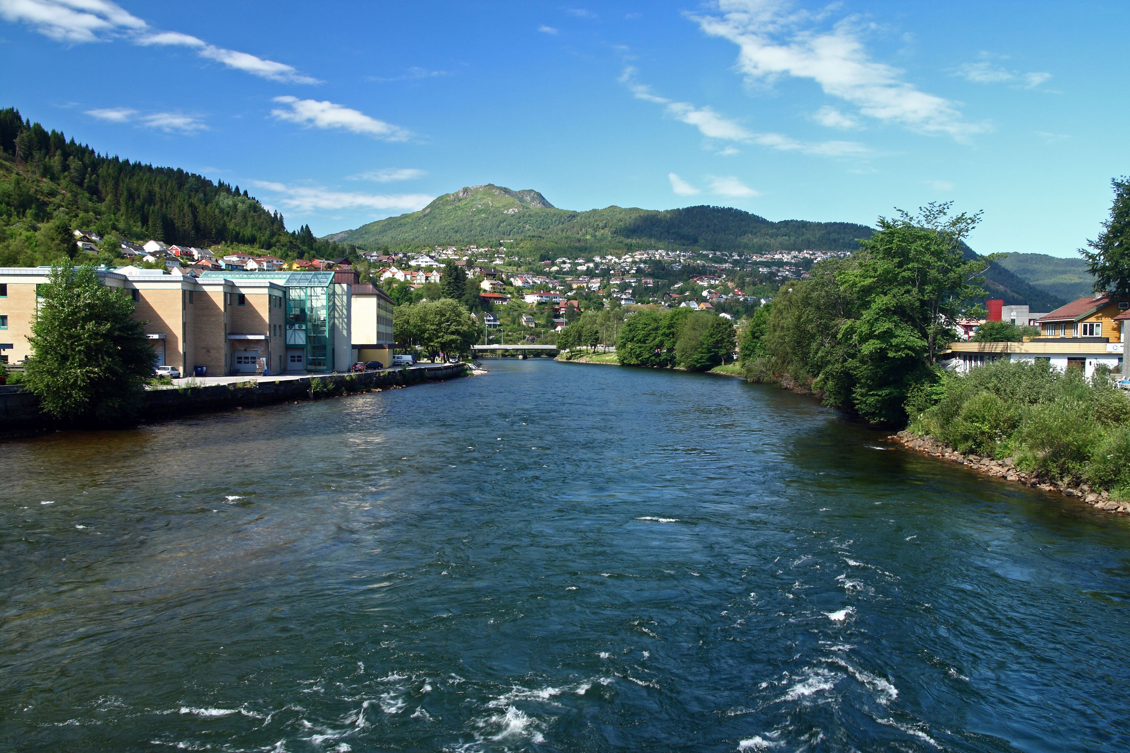 A river flowing through a town with buildings and hills in the background.