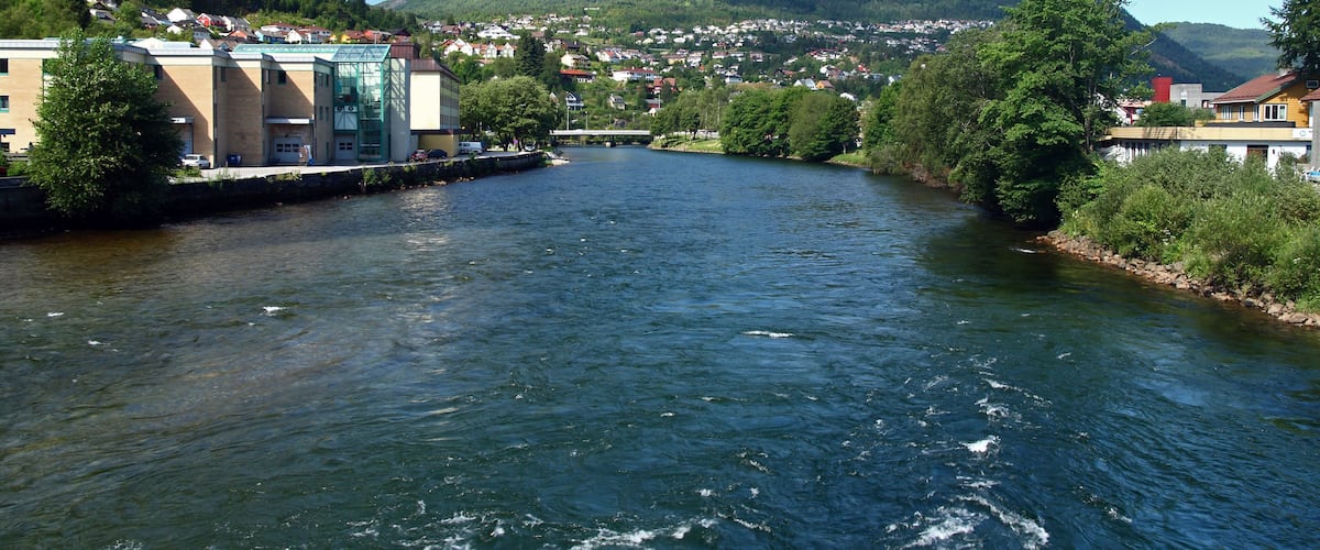 A river flowing through a town with buildings and hills in the background.