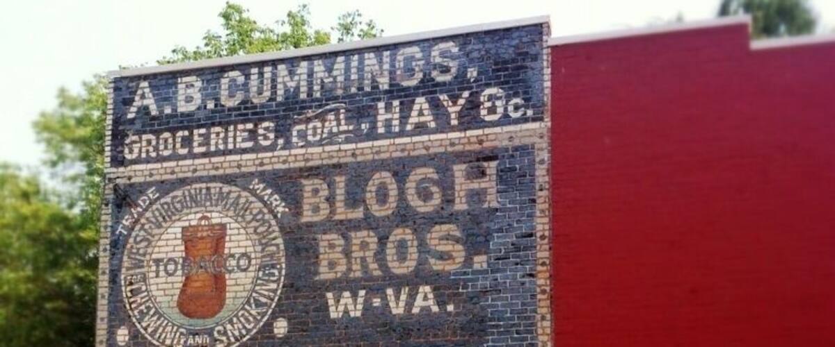 Originally built as a saloon around 1888, the Mail Pouch Building takes its name from the charming tobacco sign which graces its western wall. Restored in 1994, the sign wall is a colorful reminder of the days when sign painters toured the country covering barns and buildings with their handiwork.
Today, the building houses a unique gift and craft shop called The Crafty Peddler. Home of the 6½ ft. Cigar Store Indian carved by a local artist, this craft shop also has folk art, baskets, pottery, jewelry, home and garden décor, and Christmas creations year round.
Painted around 1895, the sign itself is made up of two parts: the lower portion, advertising Mail Pouch Tobacco, processed by Bloch Bros. of Wheeling, West Virginia. The upper portion is an advertisement for Augustus B. Cummings, who was a local businessman and possibly one of the inventors of the first plow. This portion is called a privilege panel, and was traditionally given to the building’s owner or occupant as compensation for allowing the tobacco company to paint their sign on the building.