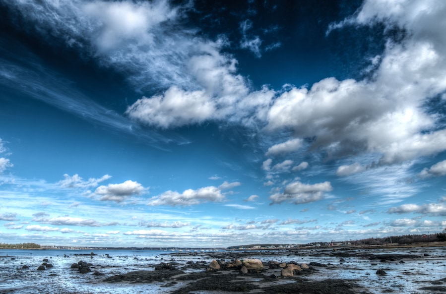 Un paysage côtier avec un ciel dégagé, quelques nuages épars et une côte rocheuse.