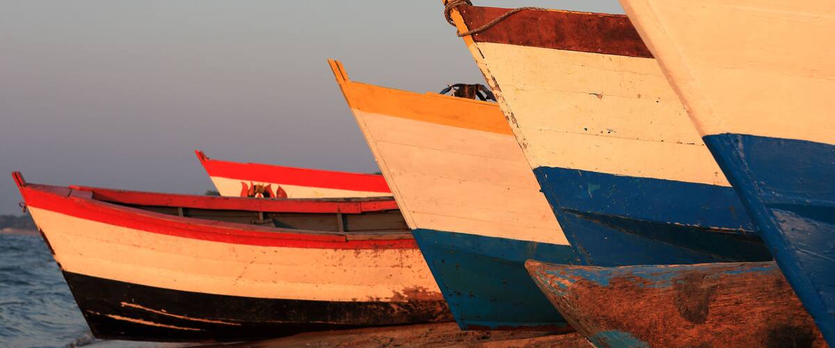 A row of colorful boats tied to a sandy beach.