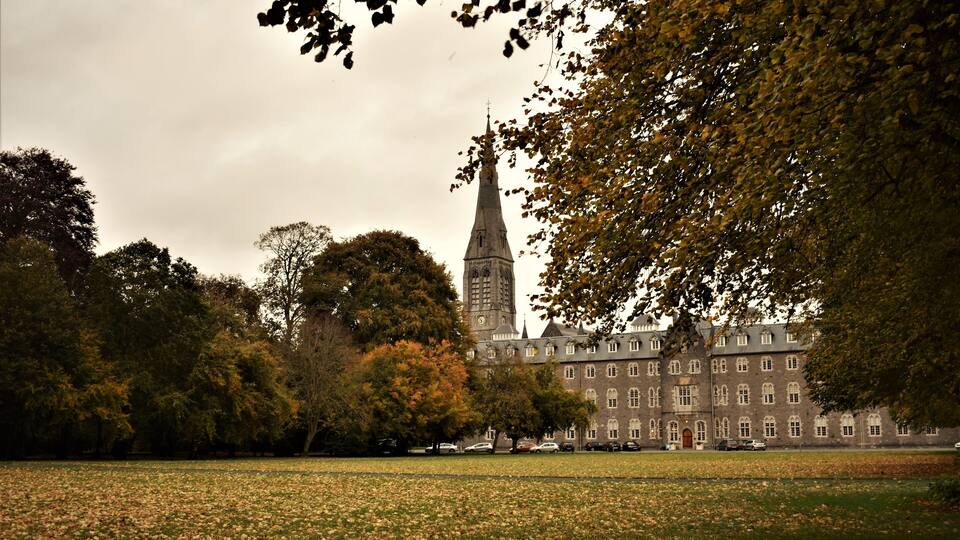 A large building with a tall spire, surrounded by trees and a grassy field.
