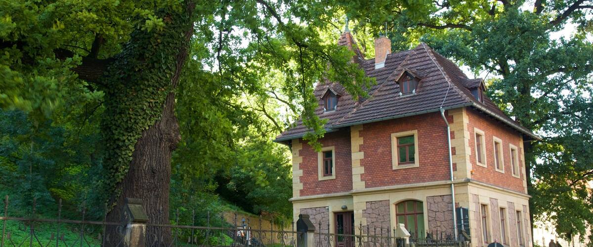 A historic building with a red brick facade, a tiled roof, and a stone wall in front.