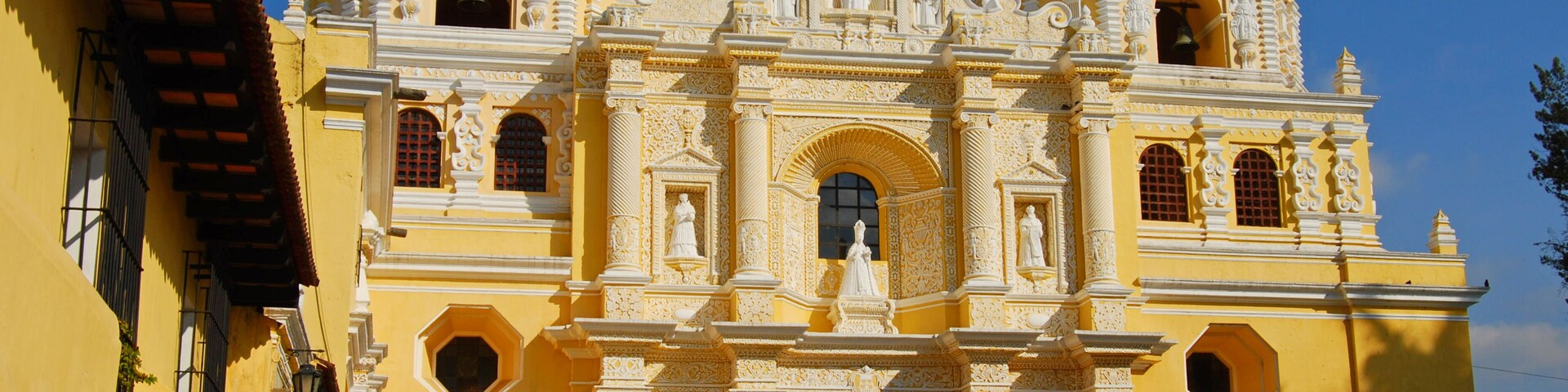 Uma igreja colonial amarela grande e ricamente decorada, com várias estátuas e arcos.